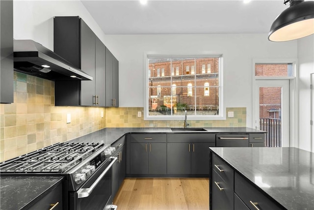 kitchen featuring dishwasher, sink, light wood-type flooring, wall chimney range hood, and gas range oven