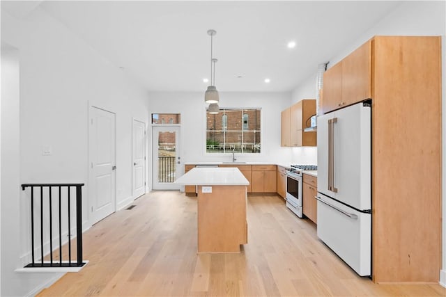 kitchen featuring light brown cabinetry, high end appliances, hanging light fixtures, light wood-type flooring, and a kitchen island