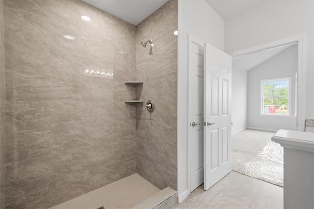 bathroom with vaulted ceiling, a tile shower, and tile flooring