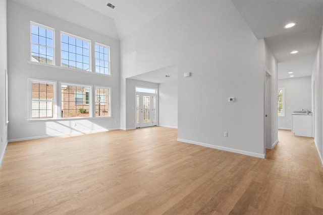 unfurnished living room featuring a healthy amount of sunlight, light hardwood / wood-style floors, and a towering ceiling