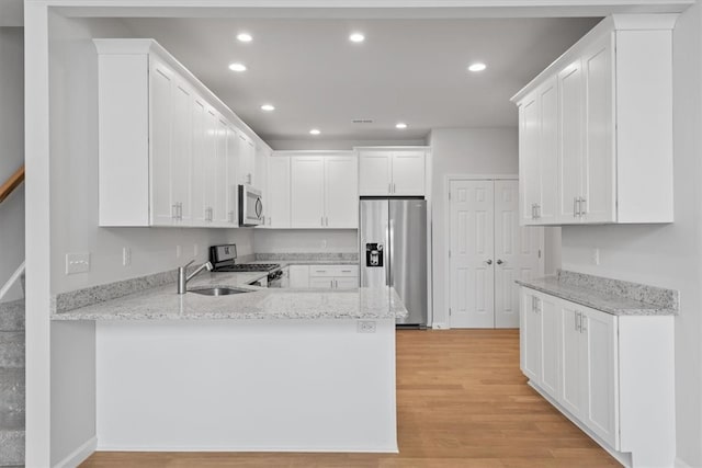 kitchen featuring white cabinets, light stone countertops, kitchen peninsula, appliances with stainless steel finishes, and light hardwood / wood-style floors