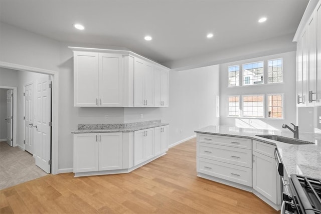 kitchen with stove, white cabinets, light stone countertops, sink, and light hardwood / wood-style floors