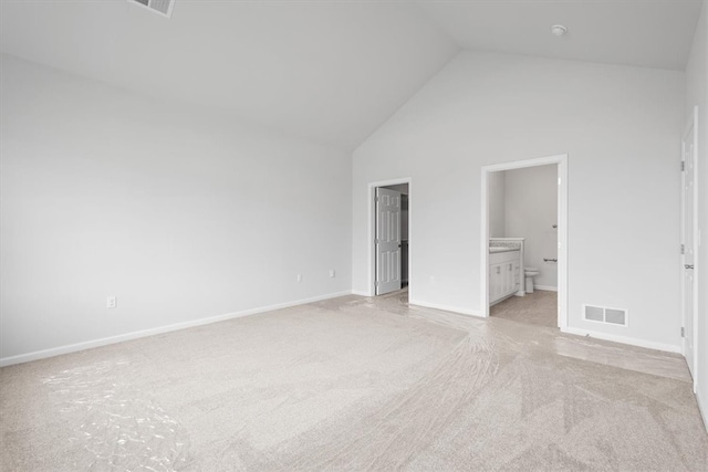 unfurnished bedroom featuring light carpet, ensuite bath, and high vaulted ceiling