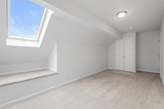 additional living space with light colored carpet and lofted ceiling with skylight