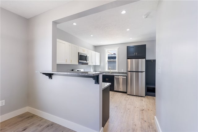 kitchen featuring a kitchen breakfast bar, kitchen peninsula, light hardwood / wood-style flooring, and stainless steel appliances