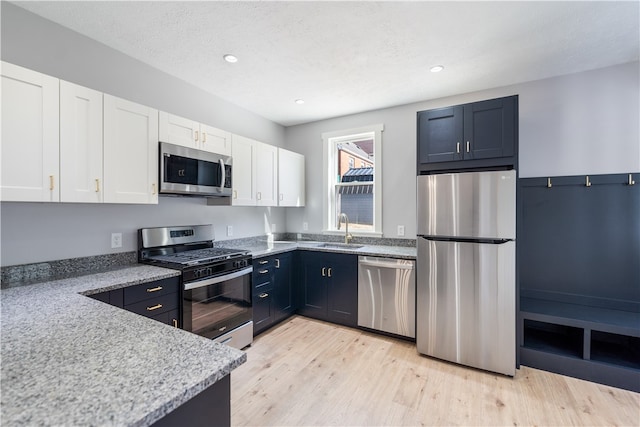 kitchen with appliances with stainless steel finishes, light stone counters, white cabinets, sink, and light wood-type flooring