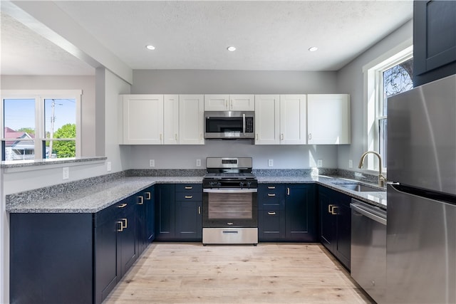 kitchen with light stone countertops, stainless steel appliances, white cabinets, sink, and light wood-type flooring