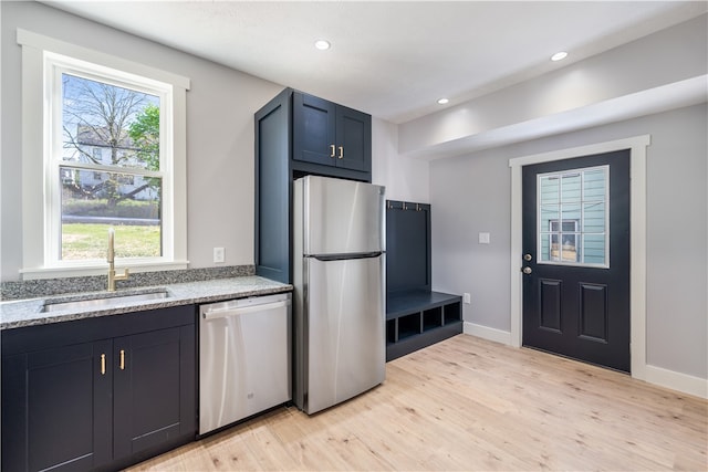 kitchen with light stone countertops, stainless steel appliances, sink, and light wood-type flooring