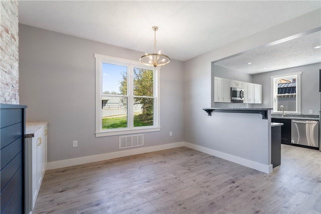 unfurnished dining area with a textured ceiling, a notable chandelier, sink, and light wood-type flooring