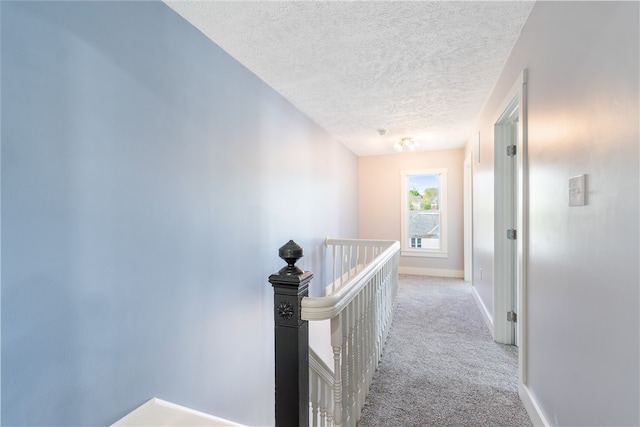 hall with light colored carpet and a textured ceiling