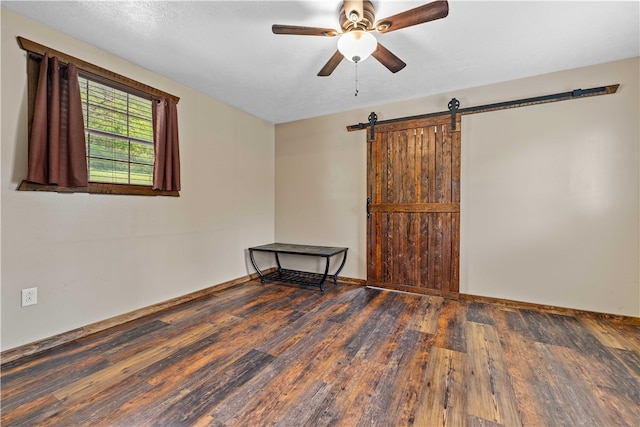 unfurnished room with a barn door, ceiling fan, and dark hardwood / wood-style floors