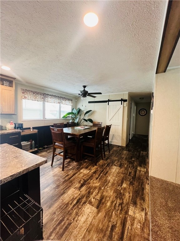 dining room with ceiling fan, a barn door, dark hardwood / wood-style floors, and a textured ceiling