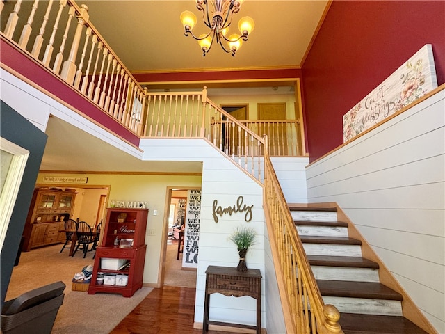 stairs featuring crown molding, a notable chandelier, a high ceiling, and hardwood / wood-style floors