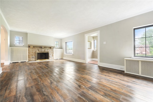 unfurnished living room with radiator, a stone fireplace, and dark wood-type flooring