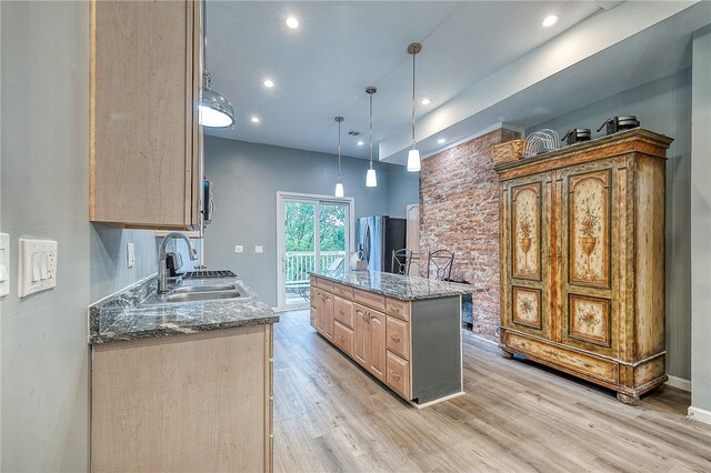 kitchen featuring light stone counters, light hardwood / wood-style floors, a center island, stainless steel fridge, and sink