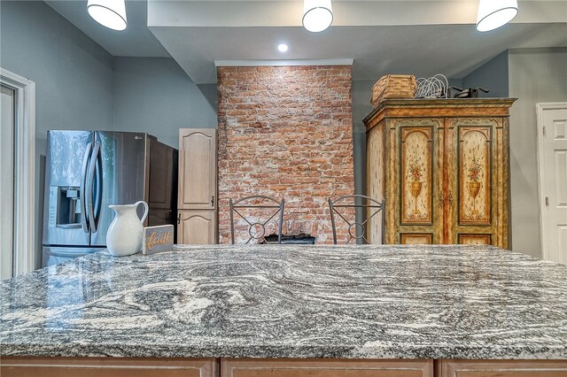 kitchen featuring vaulted ceiling, stainless steel fridge, brick wall, and dark stone countertops