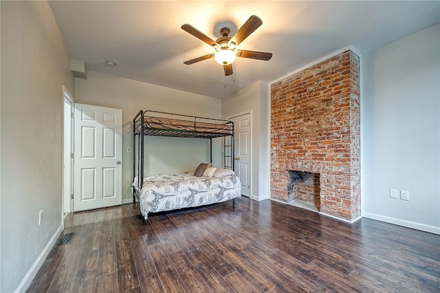 unfurnished bedroom with a brick fireplace, ceiling fan, and dark wood-type flooring