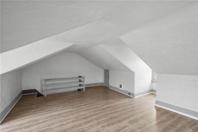 bonus room with lofted ceiling, hardwood / wood-style flooring, and a textured ceiling