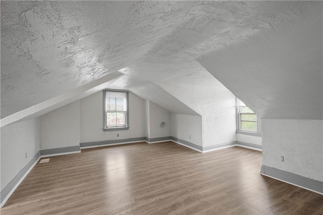 additional living space featuring a textured ceiling, hardwood / wood-style floors, and lofted ceiling