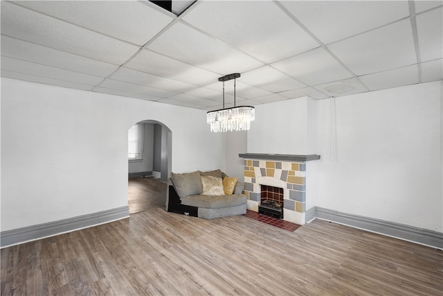 unfurnished room featuring a drop ceiling, hardwood / wood-style floors, a fireplace, and an inviting chandelier