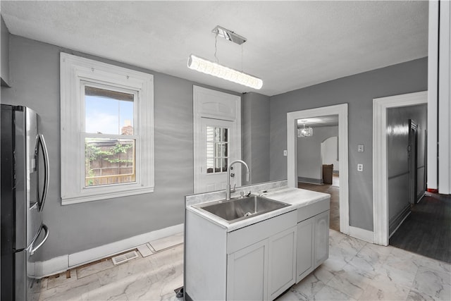 kitchen featuring hanging light fixtures, light wood-type flooring, white cabinetry, sink, and stainless steel fridge with ice dispenser