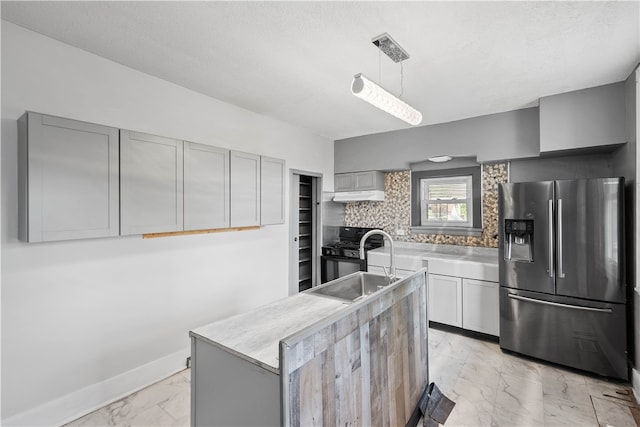 kitchen with light tile floors, tasteful backsplash, gray cabinetry, stainless steel fridge, and a center island with sink