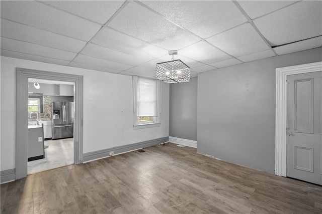 unfurnished room with wood-type flooring, a paneled ceiling, a healthy amount of sunlight, and an inviting chandelier