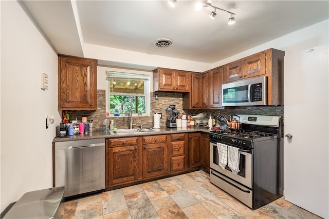 kitchen featuring light tile flooring, backsplash, appliances with stainless steel finishes, sink, and track lighting