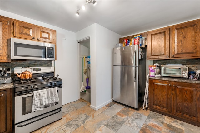 kitchen featuring rail lighting, appliances with stainless steel finishes, stone countertops, light tile floors, and tasteful backsplash