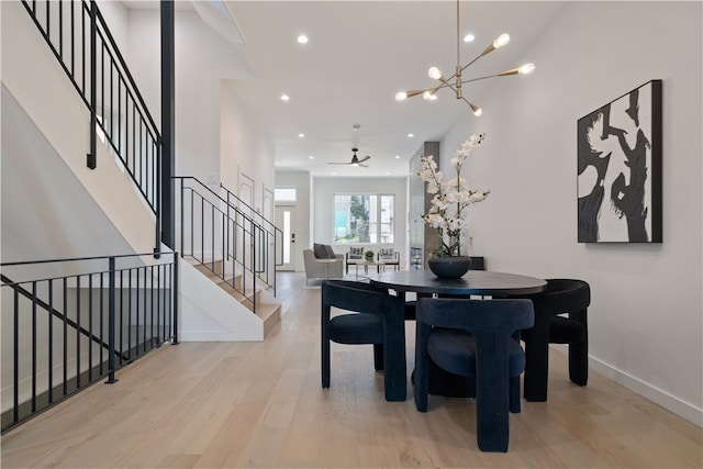 dining area featuring ceiling fan with notable chandelier, light hardwood / wood-style floors, and a towering ceiling