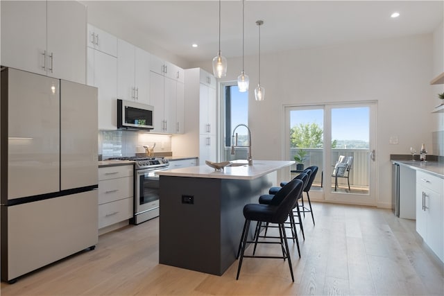 kitchen featuring white cabinets, stainless steel appliances, light wood-type flooring, and a kitchen island with sink