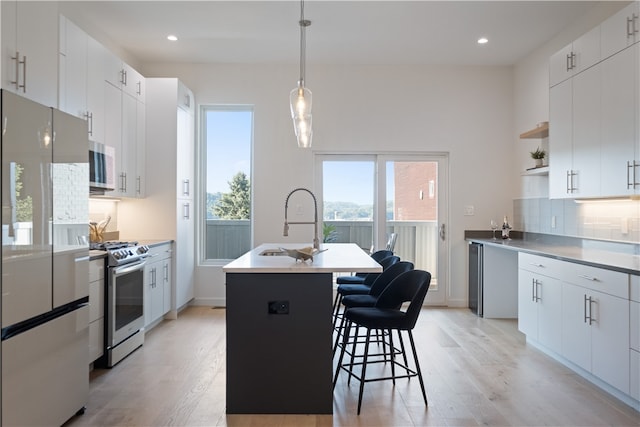 kitchen featuring appliances with stainless steel finishes, white cabinets, light hardwood / wood-style floors, backsplash, and an island with sink