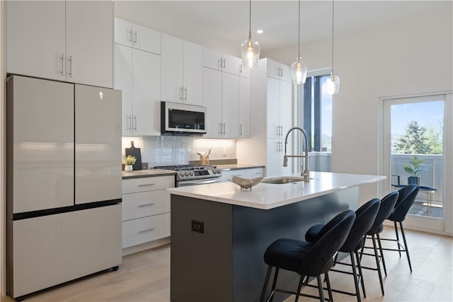 kitchen with light hardwood / wood-style floors, appliances with stainless steel finishes, an island with sink, and white cabinetry