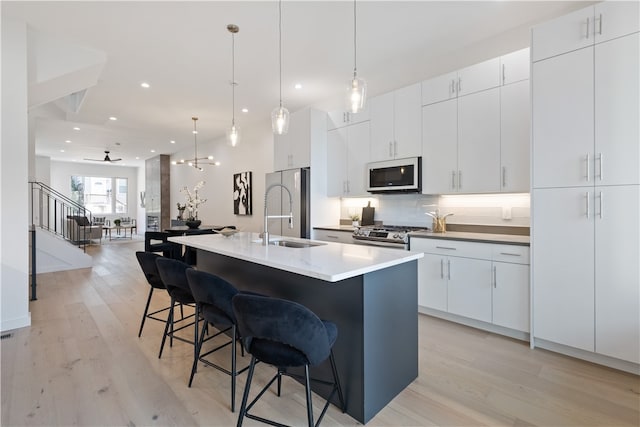 kitchen with decorative light fixtures, light hardwood / wood-style flooring, stainless steel appliances, sink, and an island with sink