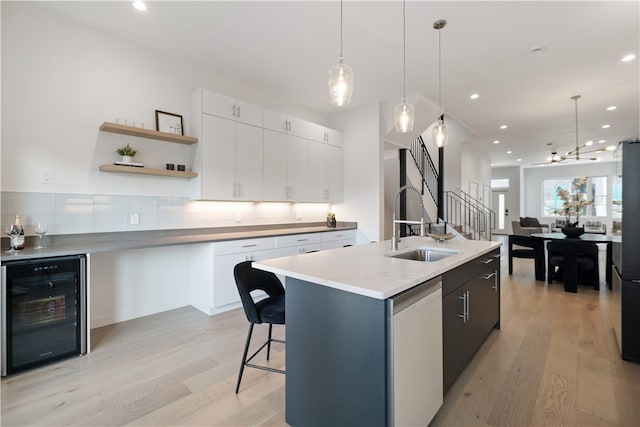 kitchen with backsplash, beverage cooler, an island with sink, white cabinets, and light wood-type flooring