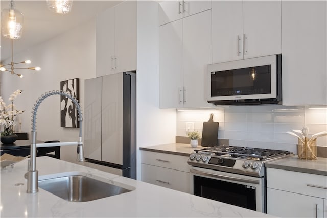 kitchen with pendant lighting, white cabinetry, backsplash, stainless steel appliances, and sink