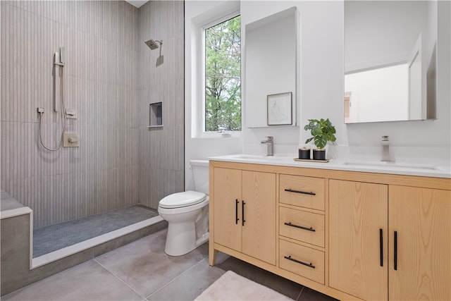 bathroom with tiled shower, a wealth of natural light, tile flooring, double sink vanity, and toilet