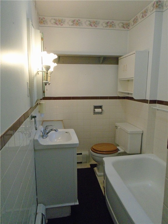 bathroom with baseboard heating, toilet, vanity, and tile walls