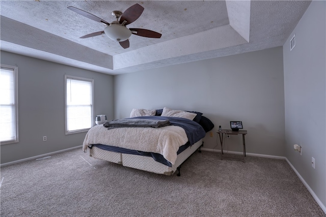 carpeted bedroom with ceiling fan, a raised ceiling, and a textured ceiling