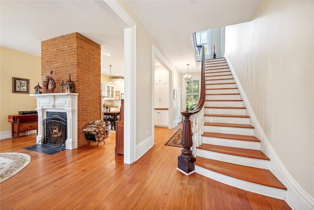 stairs with brick wall, a notable chandelier, and light hardwood / wood-style flooring