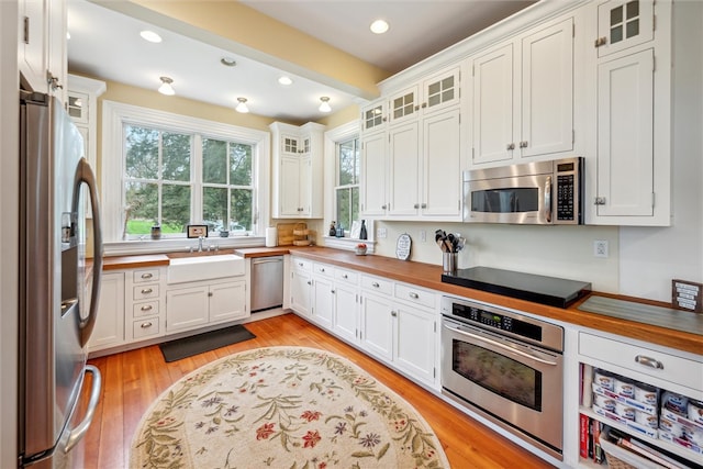 kitchen with stainless steel appliances, white cabinetry, beam ceiling, light wood-type flooring, and sink