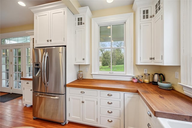 kitchen with stainless steel refrigerator with ice dispenser, white cabinets, light hardwood / wood-style flooring, and wood counters