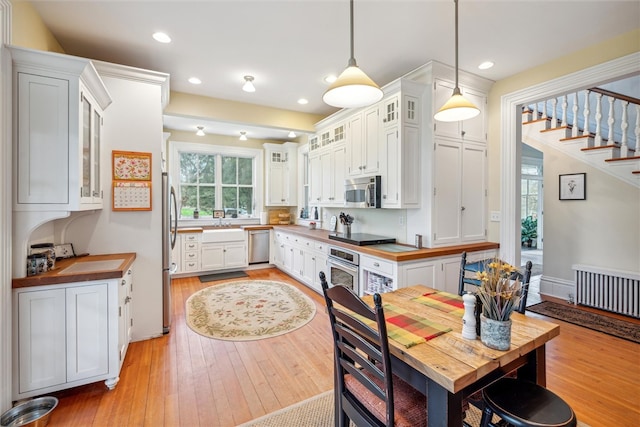 interior space featuring light hardwood / wood-style floors, butcher block countertops, hanging light fixtures, white cabinetry, and appliances with stainless steel finishes