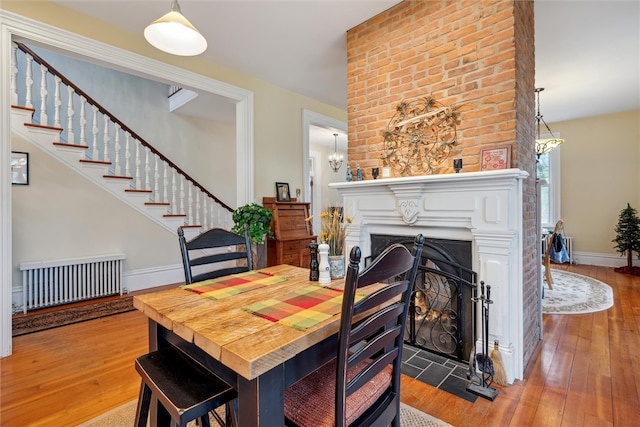 dining space featuring a notable chandelier, hardwood / wood-style flooring, brick wall, and radiator