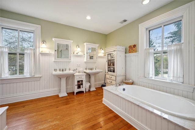 bathroom with a relaxing tiled bath, wood-type flooring, and sink