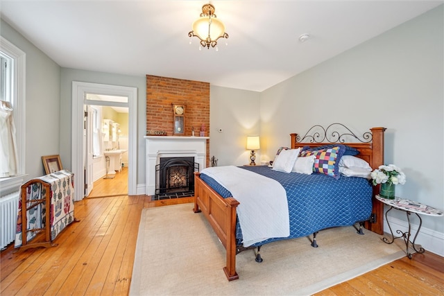 bedroom featuring brick wall, ensuite bath, and light hardwood / wood-style flooring