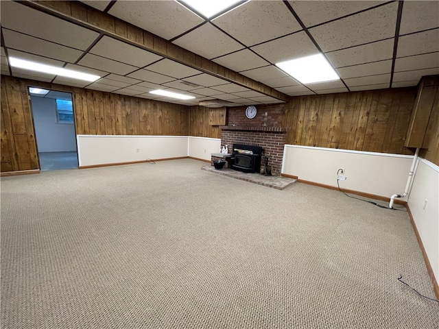 basement featuring carpet flooring, a paneled ceiling, and a wood stove