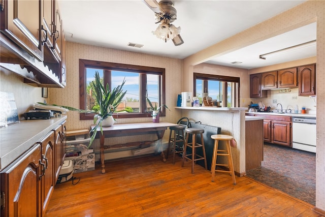 kitchen with wood-type flooring, ceiling fan, a kitchen breakfast bar, and white dishwasher