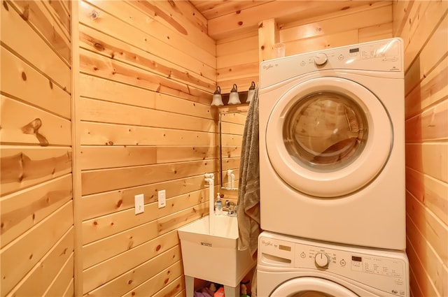 clothes washing area with wood ceiling, sink, stacked washer and dryer, and wooden walls