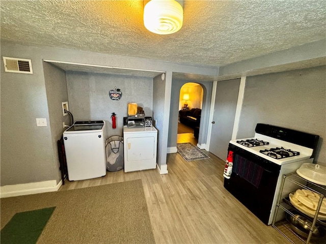 kitchen featuring a textured ceiling, range with gas stovetop, washing machine and clothes dryer, and light wood-type flooring